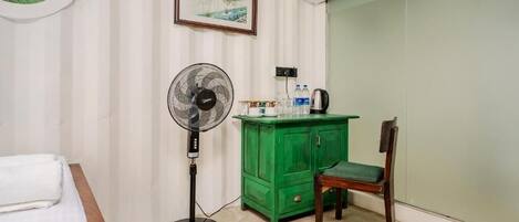 A hotel room with a bed, a standing fan, a green cabinet, and a chair.