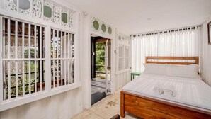 A bedroom with a wooden bed, white curtains, and a view of the garden through a window with decorative white panels. - Secret Beach Ahangama Galle (Ahangama)