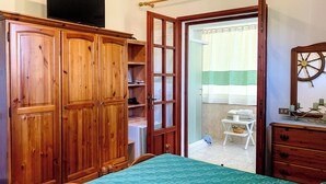 A bedroom with a bed, wooden wardrobe, and a bathroom visible through an open door. - VILLA GISA (Domus de Maria)