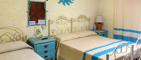 A bedroom with two beds, a nightstand with a lamp, a wall-mounted air conditioner, and a decorative wall piece.