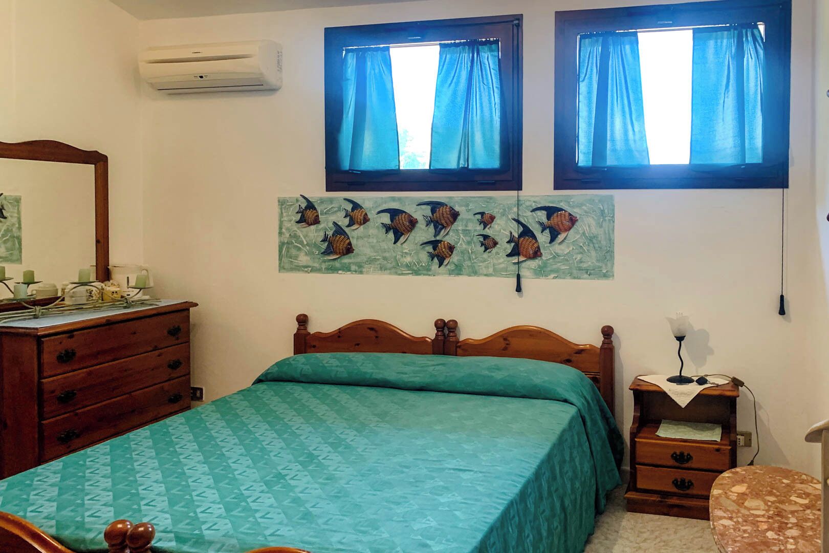 Un dormitorio con cama, cómoda, mesita de noche, lámpara y aire acondicionado instalado en la pared.
