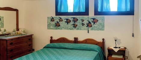 Un dormitorio con cama, cómoda, mesita de noche, lámpara y aire acondicionado instalado en la pared.