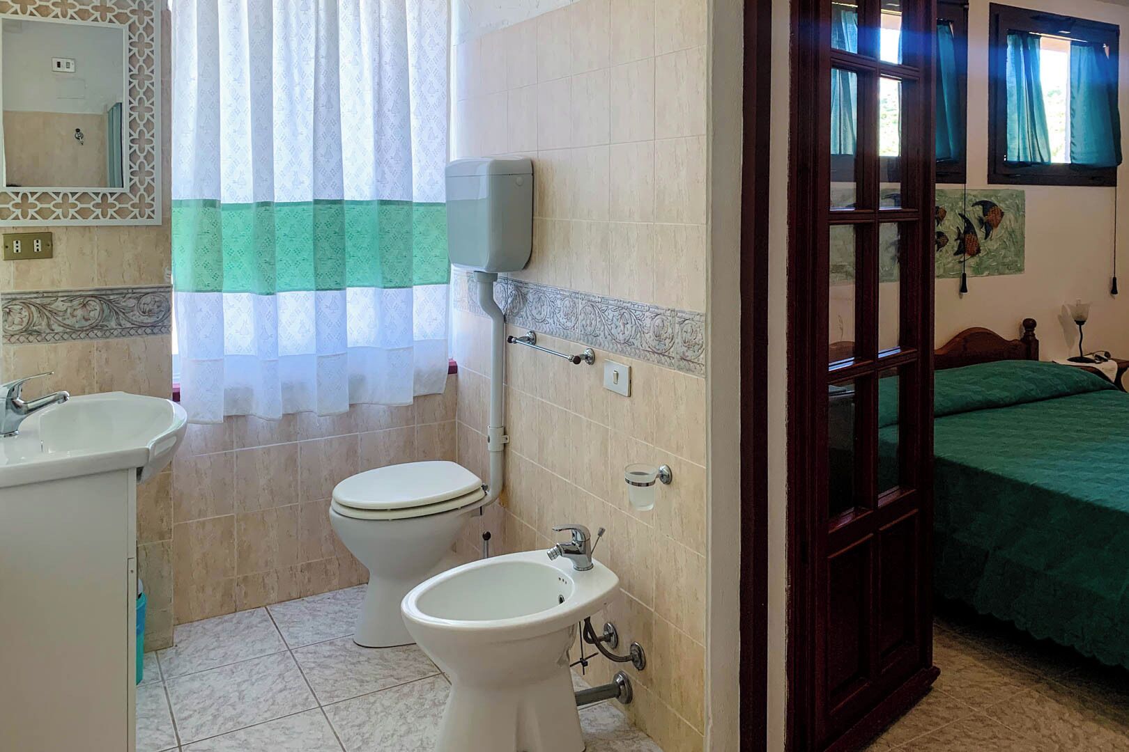 A bathroom with a toilet, bidet, sink, and a mirror.