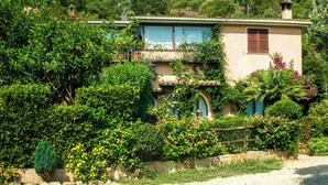 A two-story house with a garden, surrounded by trees and hills. - VILLA GISA (Domus de Maria)