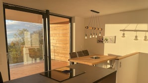 A modern kitchen with a wooden dining table, a built-in oven, and a large window overlooking a deck. - Eichen-Chalet (Eichenberg)