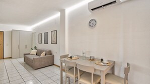 Un salon moderne comprenant un coin repas, des murs blancs, un canapé, une table avec des chaises et un appareil de climatisation.