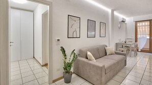 Un salon avec un canapé beige, une table à manger avec des chaises, une plante en pot et des œuvres d’art encadrées accrochées au mur.
