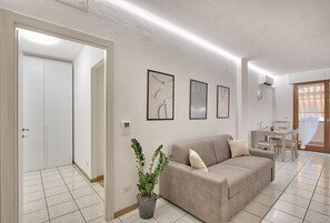 Ein Wohnzimmer mit beiger Couch, einem Esstisch mit Stühlen, einem Blumentopf und gerahmten Kunstwerken an der Wand.