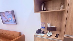 A hotel room with a wooden cabinet, a small refrigerator, a sofa, and a wall-mounted television. - Sonder Hau Giang Hotel (Ho Chi Minh City)