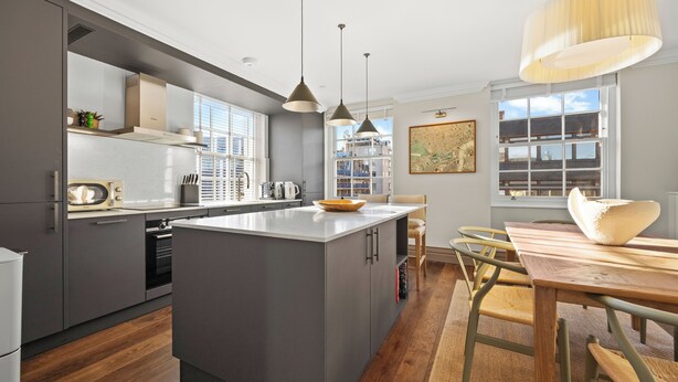 Una cocina moderna con una isla central, una mesa de comedor de madera e iluminación colgante.