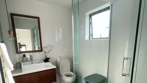 Un bany modern amb una cabina de dutxa de vidre, un lavabo blanc i un vàter.