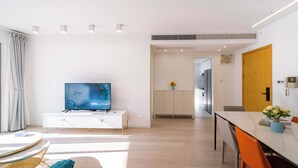 Ein modernes Wohnzimmer mit einem Flachbildfernseher, einem Esstisch und einer Küchenzeile im Hintergrund.
