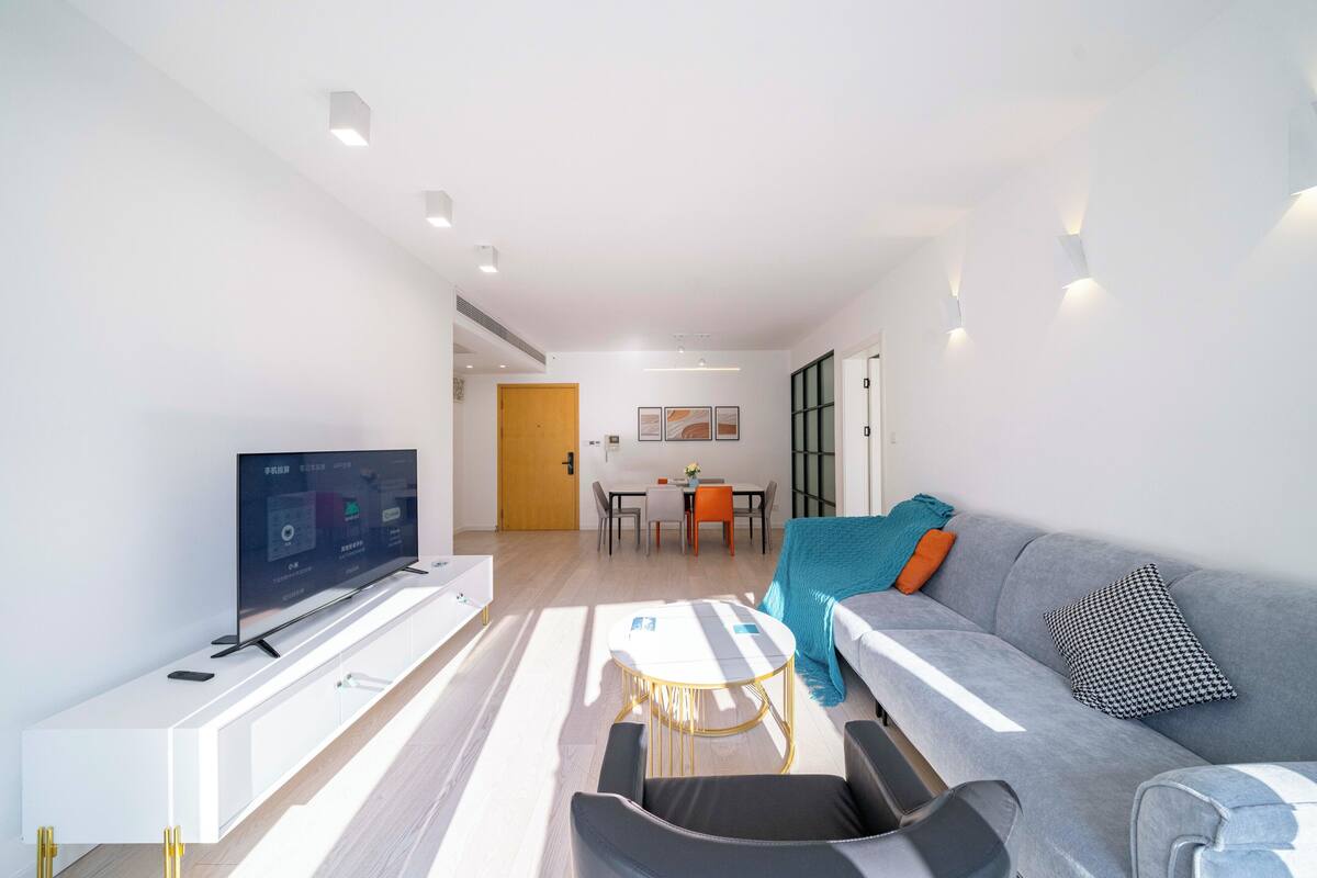 Een moderne woonkamer met een flatscreen televisie, een bank, een salontafel en een eethoek op de achtergrond.