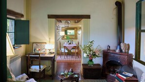 A cozy living room with a fireplace, a dining area with a table set for two, and a view into another room with a bed and a window. - Il Gallinaio, Vivo D'Orcia (Vivo D'orcia)
