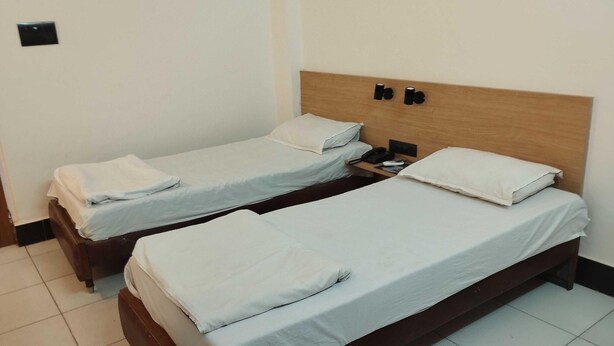 Two single beds with wooden headboards, white bedding, and a bedside table with a phone and remote control. - Townhouse Naksalbari Railway Station (Siliguri)