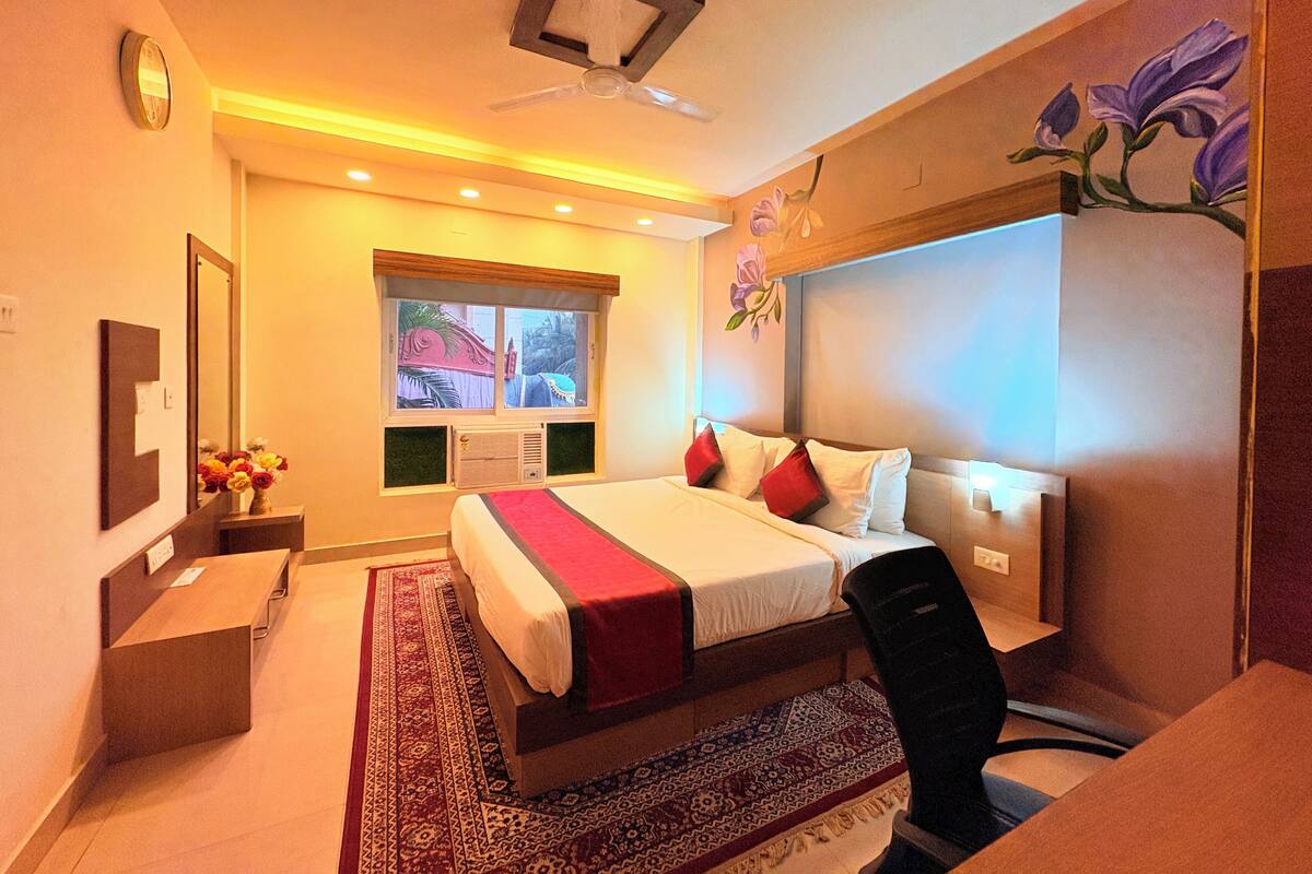 A hotel room with a bed, a desk, a chair, a window with a view, a ceiling fan, and a wall-mounted air conditioner.