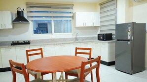 A kitchen with white cabinets, a wooden table with four chairs, a stainless steel refrigerator, and a microwave. - AM SUITES LUXURY SERVICE APARTMENTS (Hyderabad)