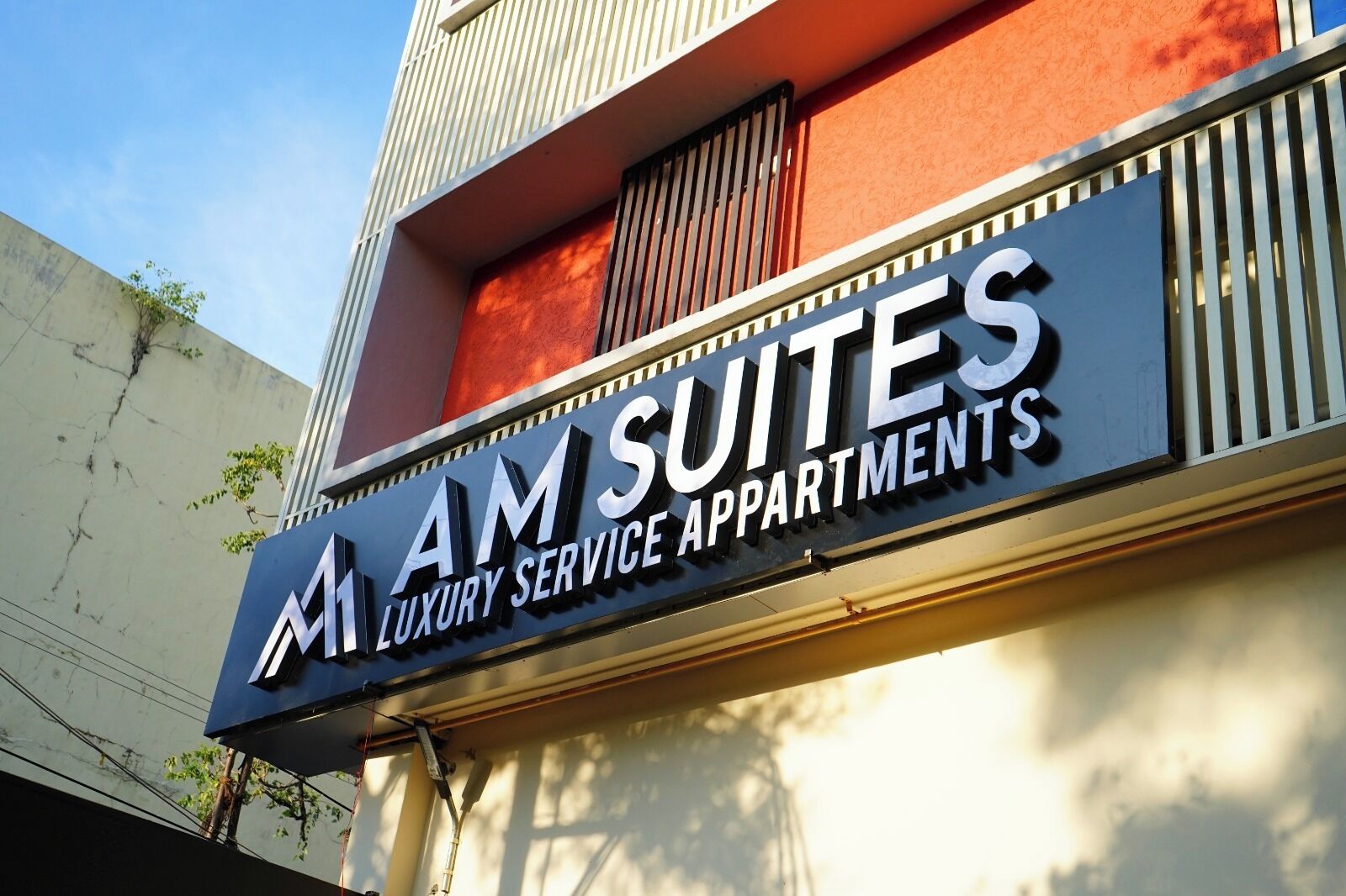 Señalización de 'AM SUITES LUXURY SERVICE APARTMENTS' con un diseño moderno y un balcón.