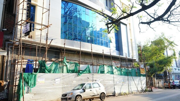 A building under construction with scaffolding and green netting. - AM SUITES LUXURY SERVICE APARTMENTS (Hyderabad)
