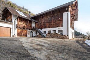 Ein großes, auf einem Bauernhof typisches Gebäude mit einer Treppe zum Obergeschoss, einer Garage und einem Holzstapel.
