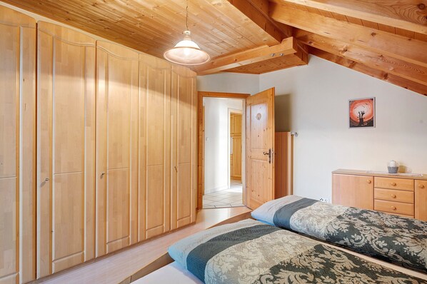 A bedroom with a bed, wooden wardrobe, and a door leading to another room.