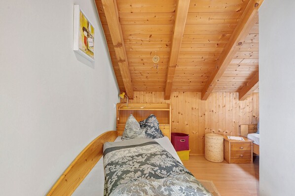 A wooden ceiling, a bed with pillows, a nightstand, a trash bin, and a wall-mounted picture. - Holiday Apartment Ebnicher's Paradise – Retreat with Shared Terrace, Garden and Wi-Fi (Soprabolzano/Renon)