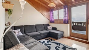 A modern living room with a sectional sofa, a hanging light fixture, and a large window with a view. - Holiday Apartment Ebnicher's Paradise – Retreat with Shared Terrace, Garden and Wi-Fi (Soprabolzano/Renon)