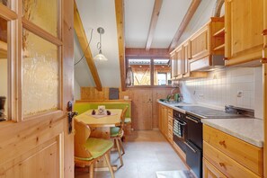 Eine kleine Küche mit Holzschränken, einem Esstisch mit Stühlen und einem Fenster mit Vorhängen.