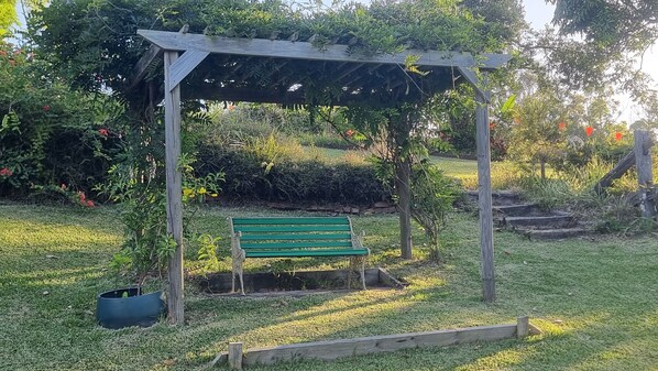 A wooden pergola with a bench underneath, surrounded by lush greenery and a garden. - Belle Vue-River front in Urunga-peaceful, amazing views, bird song. Small dog OK (Urunga)