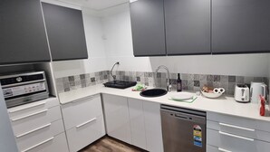 Moderni keittiö, jossa on valkoiset kaapit, musta työtaso, ruostumattomasta teräksestä valmistettu astianpesukone, pesuallas ja leivänpaahdin.