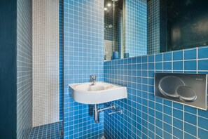 A bathroom with blue tiled walls, a white sink, and a mirror. - Chic 1BR in the Heart of Le Marais - Bretagne (Paris)