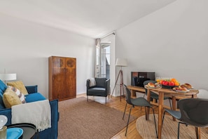 Una sala moderna con un sofá azul, un aparador de madera, una mesa de comedor con sillas y una pequeña zona de cocina.