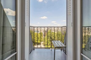 Un balcón con barandilla de metal, una mesita y vistas a la ciudad.