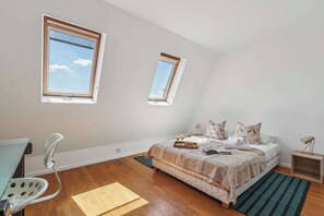A bedroom with a bed, two windows, a chair, a desk, and a nightstand. - Chic 1BR in the Heart of Le Marais - Bretagne (Paris)
