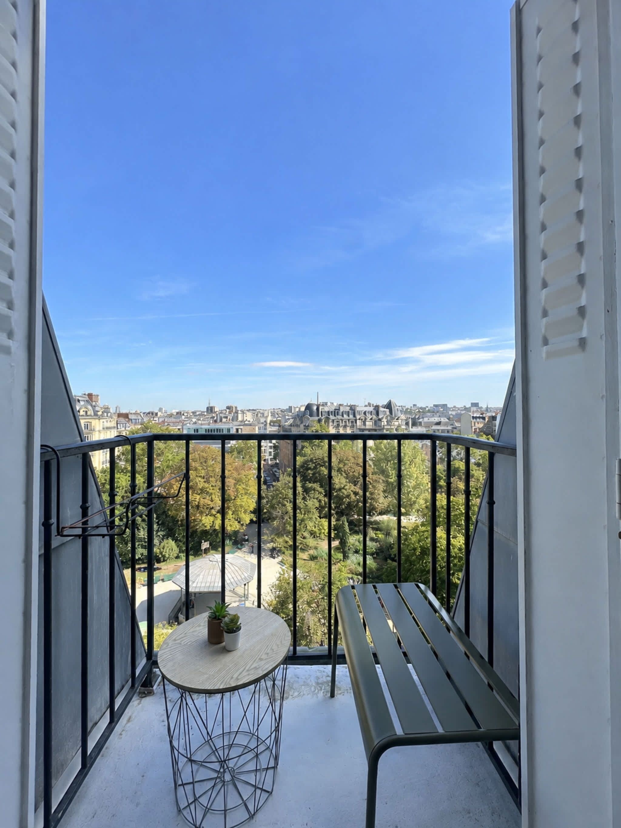 A balcony with a view of a cityscape, a round table with a small plant, and a bench.