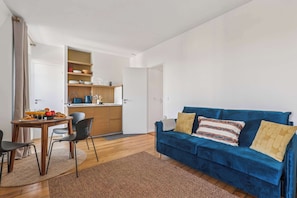Un espacio habitable compacto con comedor, kitchenette y un sofá azul con cojines.