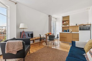 A modern apartment with a living room, dining area, and kitchen. It features a sofa, a dining table with chairs, a kitchen counter, and a large window. - Chic 1BR in the Heart of Le Marais - Bretagne (Paris)