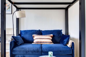 Ein blaues Sofa mit gestreiften Kissen, eine Lampe und ein kleiner Tisch mit einer Tasse.