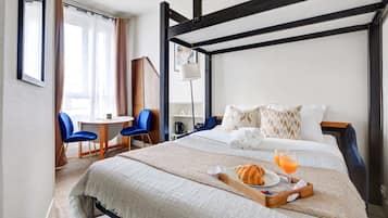 Habitación de hotel con cama, bandeja de desayuno y escritorio con sillas.