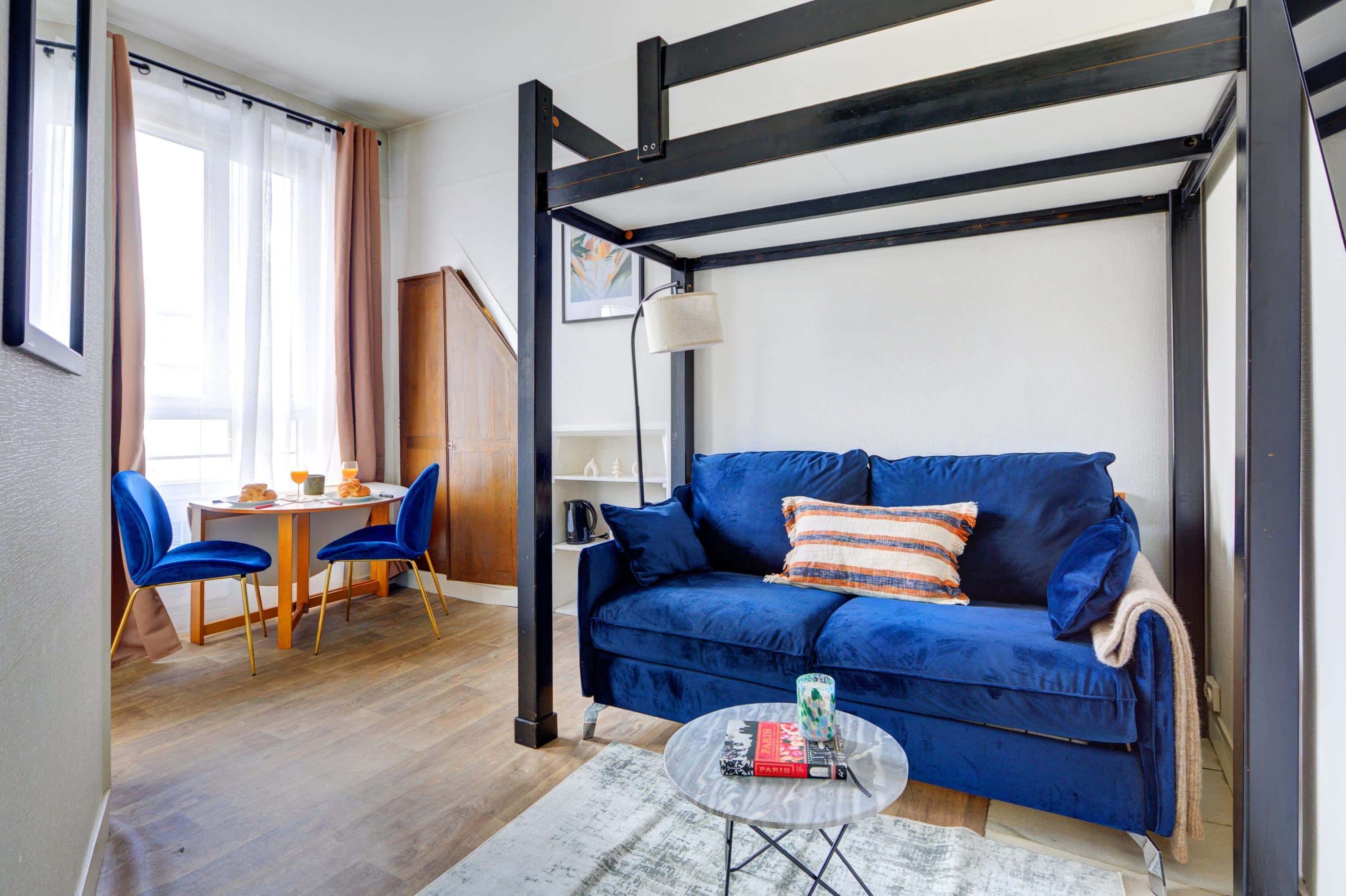 Et moderne værelse med en blå sofa, et spisebord med stole og en hængende lampe.