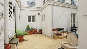 A narrow courtyard with a traditional outdoor toilet, potted plants, and a small window. - Stylish 1BR by Les Invalides & Eiffel Tower (Paris)