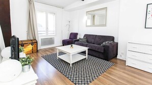 A modern living room with a sofa, a coffee table, a chest of drawers, and a patterned rug. - Le Marais - 1BR by Pompidou (Paris)