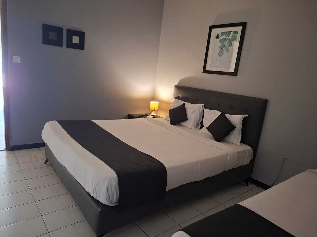 A neatly made bed with a black and white bedspread, a bedside lamp, and a framed picture on the wall.