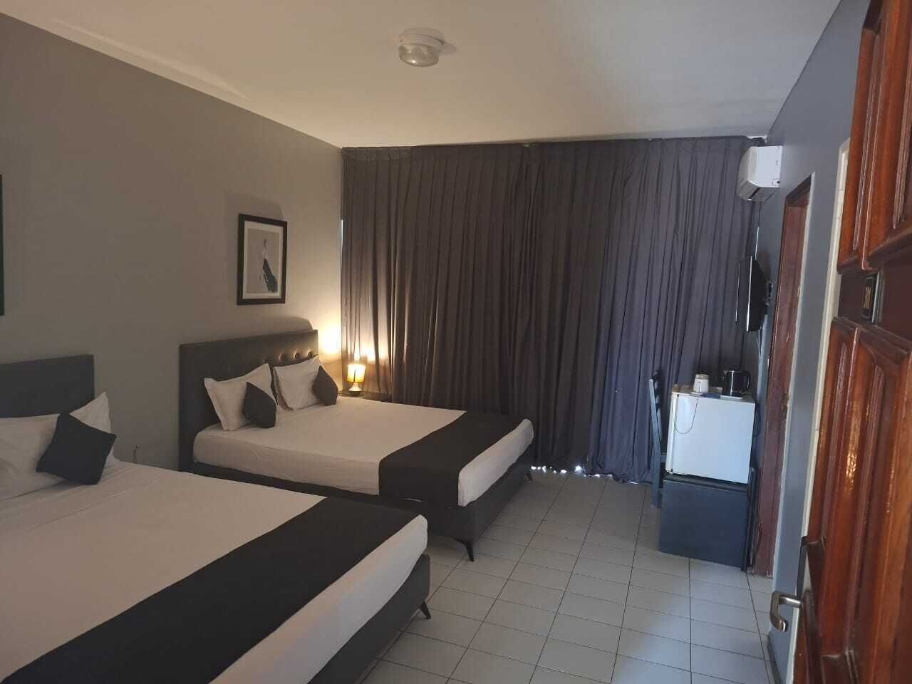 A hotel room with two beds, a small kitchenette, and a large window with curtains.