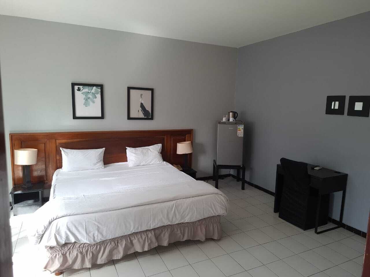 Una habitación de hotel con una cama grande, dos mesitas de noche con lámparas, un escritorio pequeño y un refrigerador.
