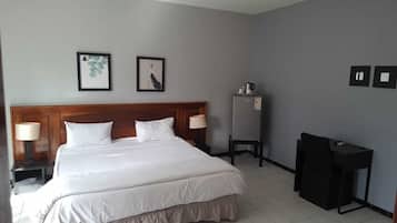 Una habitación de hotel con una cama grande, dos mesitas de noche con lámparas, un escritorio pequeño y un refrigerador.