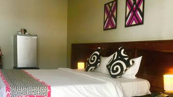 A hotel room with a bed, bedside lamps, a nightstand, a refrigerator, and two wall art pieces.