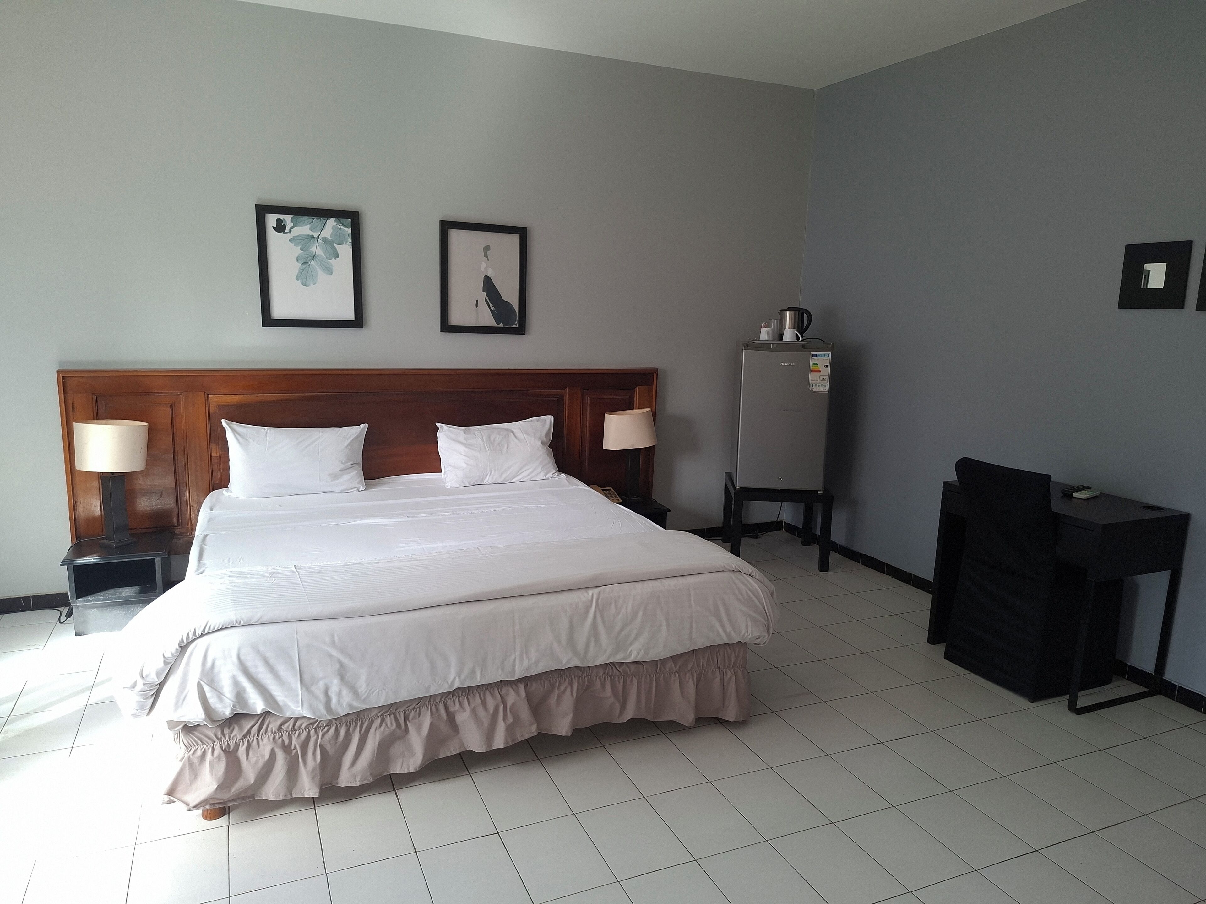 Een hotelkamer met een groot bed, twee bedlampen, een koelkast en een bureau met een stoel.