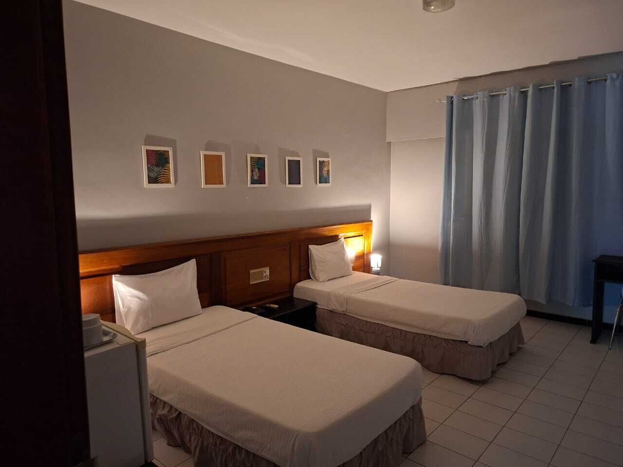 A hotel room with two single beds, a wooden headboard, a desk, and a chair.