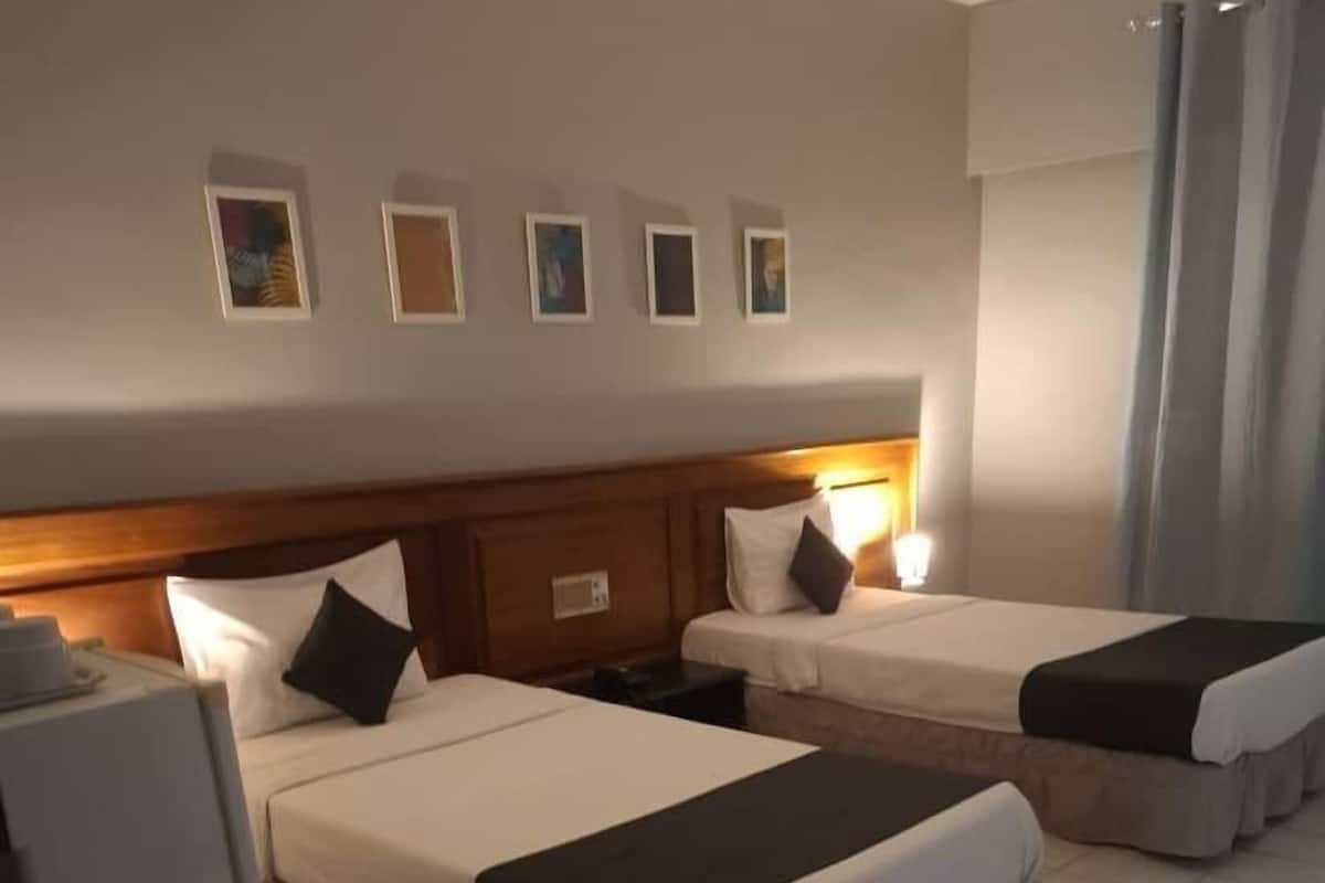 Une chambre d’hôtel avec deux lits, une tête de lit en bois, une table de chevet et une lampe fixée au mur.